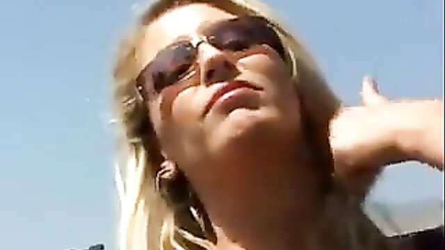 Blonde MILF in shades flashes thumbs up outdoors, ready to fuck