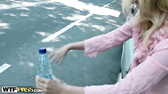 Blonde babe in pink top holding water bottle by car outdoors
