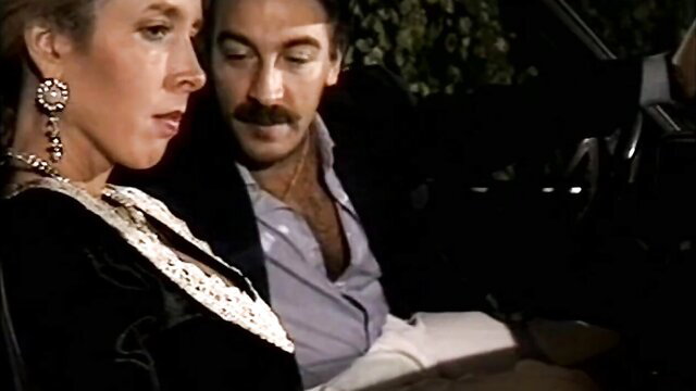 90s blonde MILF in black dress cuddles mustached man in car