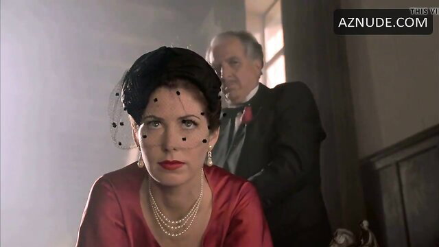 Vintage brunette in red silk dress stares intensely with suited man behind
