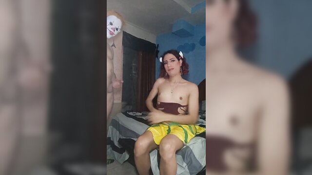Real femboy topless in yellow shorts on bed with clown cutout