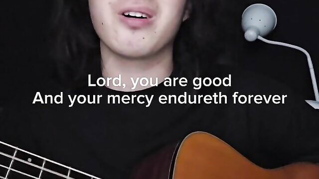 Asian male singer with long hair strums guitar, lips parted in song