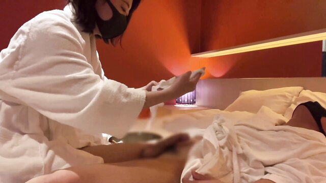 Japanese woman in robe gives lotion handjob to man on bed