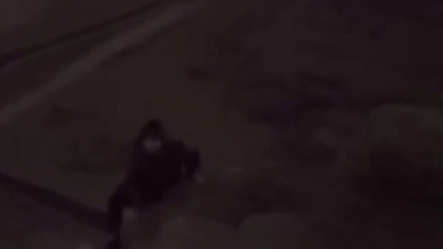 Blurry night video of masked man in dark clothes crouching outdoors