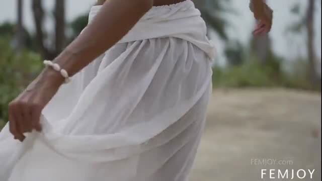 Tanned beauty in sheer white sarong on beach, revealing natural curves