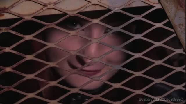 Elizabeth Thorn peeking through rusty cage bars in bondage