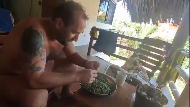 Bald bearded man preparing food in a tropical setting