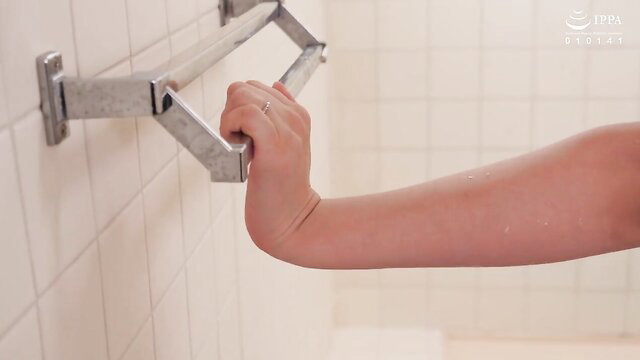 Yuki Kona gripping grab bar in shower, nude arm visible