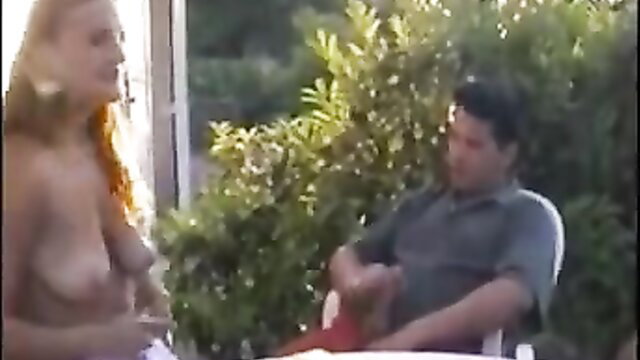 Busty blonde topless with Latino man outdoors in garden