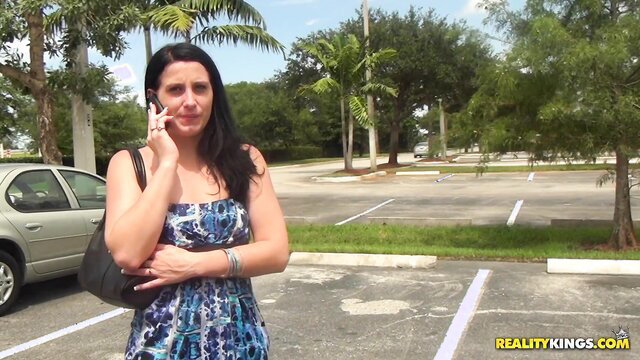Hot brunette Nikki in floral dress talks on phone in parking lot
