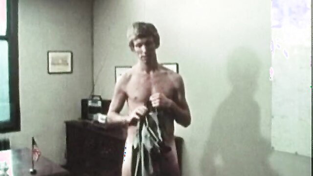 Nude 70s hunk with shaggy hair holding towel in vintage gay porn scene