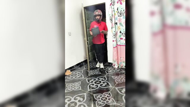 Becky Carol as Valeria Castañeda in red shirt, delivery helmet, bathroom mirror selfie