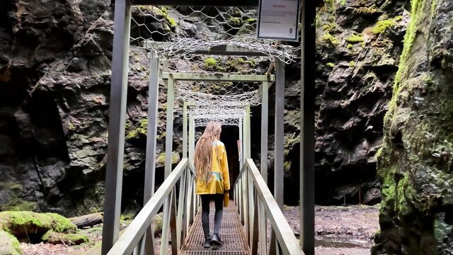 Implantboy in yellow raincoat on bridge entering lush cave tunnel