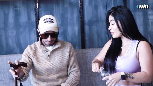Alejandra Palacios with man in hat on couch, blindfold sex tease