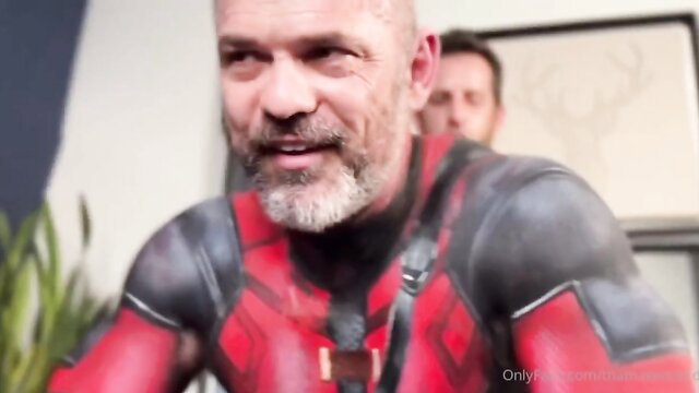 Bald bearded man in Deadpool bodypaint with another man, Halloween gay scene