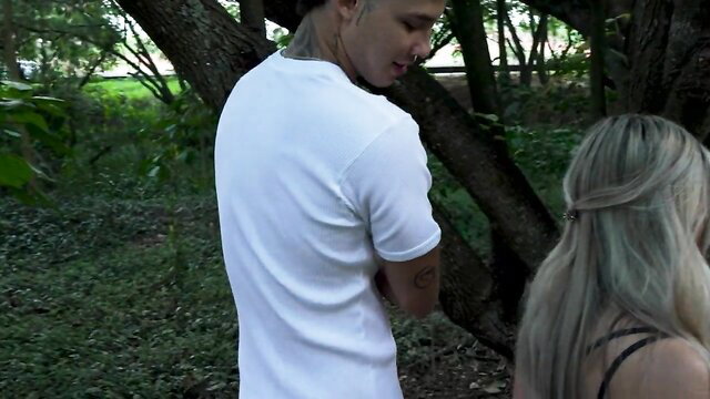 Naty Delgado walks behind tattooed Danner Mendez in park woods