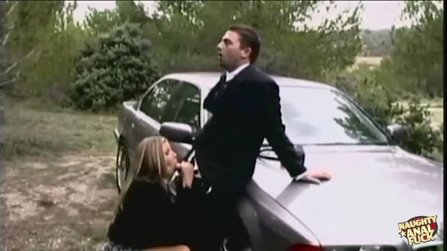Blonde woman giving oral sex to suited man on silver car outdoors