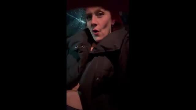 Woman in winter jacket outdoors at night showing surprised expression