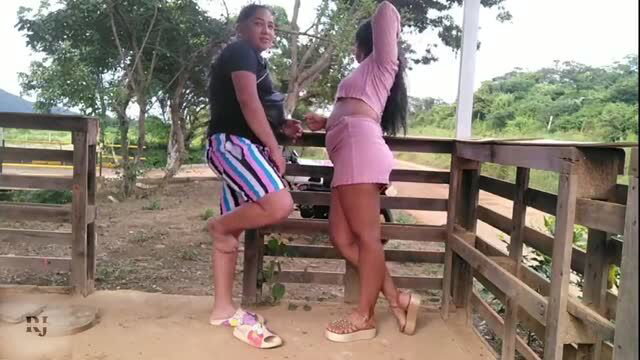 Two curvy Latina women posing by wooden fence in pink and black outfits