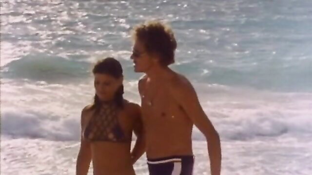 Vintage 1977 beach couple: busty brunette in bikini with shirtless hunk