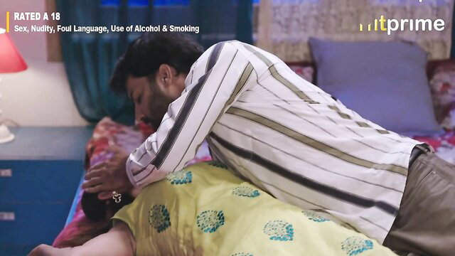 Indian couple in bed, man kissing neck of woman in yellow dress from behind