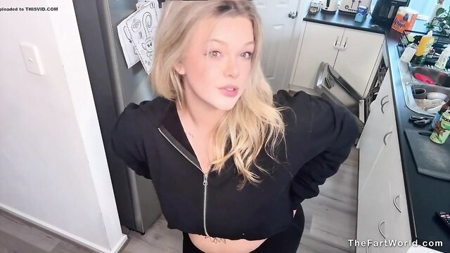 Blonde girl in crop hoodie smiles playfully in kitchen fart video thumbnail