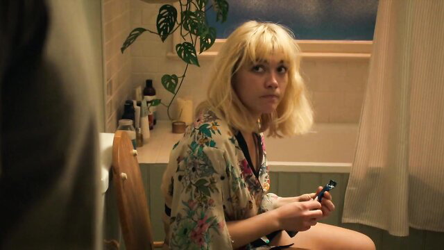 Florence Pugh in sheer floral robe, blonde bangs, sitting nude in bathroom