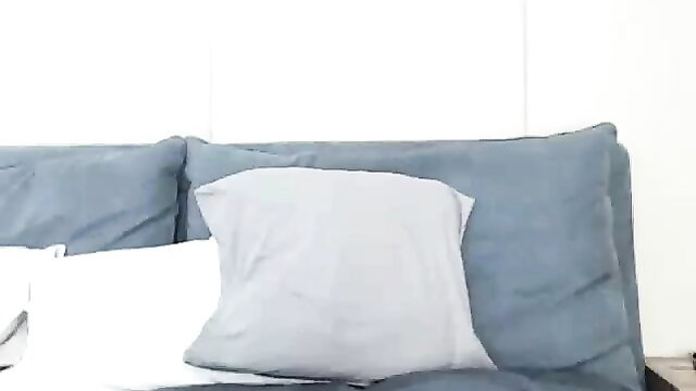 Busty chick teases with pillows on blue couch in sexy cam pose