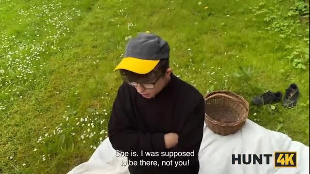 Young man in cap sitting on blanket in grass, basket nearby, subtitle text visible