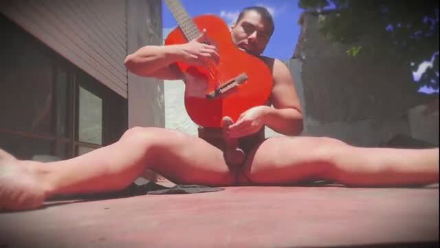 Muscular man outdoors with red guitar on naked penis, legs spread wide