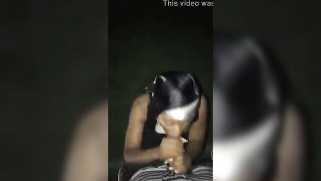 Blurry amateur girl kneeling outdoors at night, hands near mouth, blowjob tease