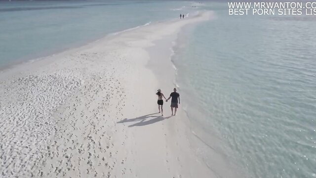 Hot couple walks hand-in-hand on tropical sandbar beach