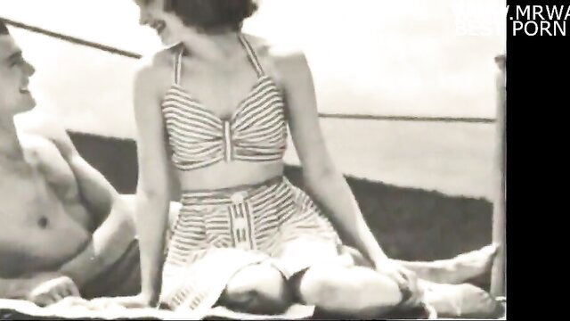 Vintage 1950s black and white couple on beach, smiling woman in striped bikini