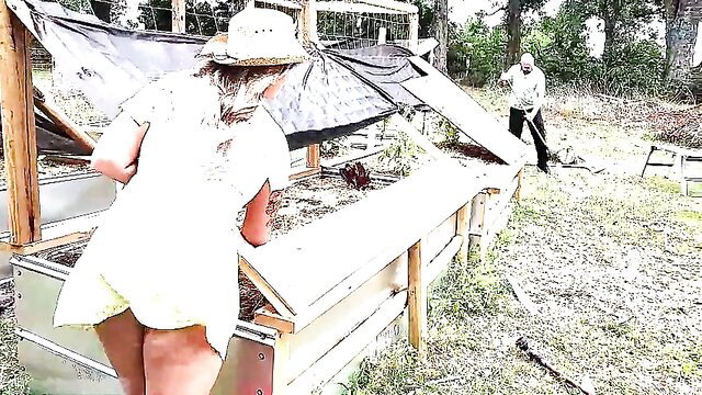 Blonde MILF in short white dress bends over chicken coop outdoors with old landscaper
