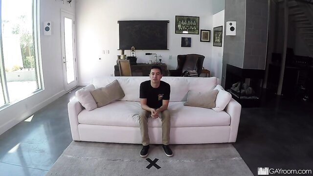 Johnny Cruz sits clothed on sofa in Gay Castings audition