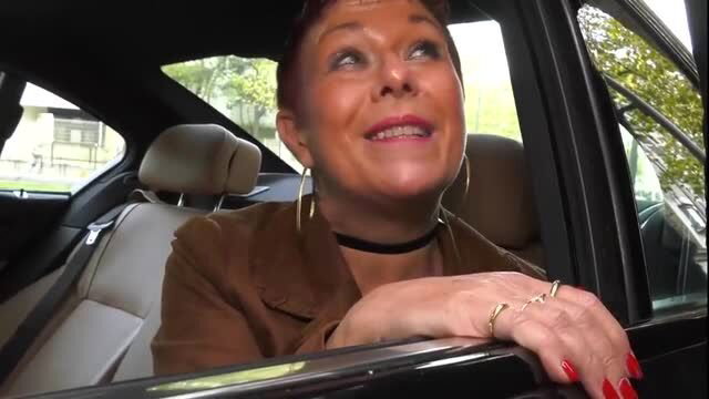 60yo redhead cougar smiling in car, choker and hoop earrings