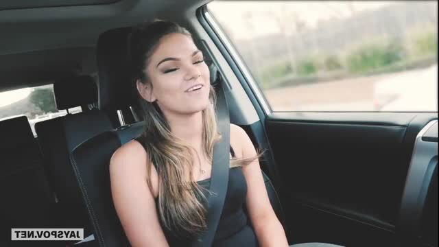 Athena Faris in car wearing black dress and seatbelt, smiling seductively