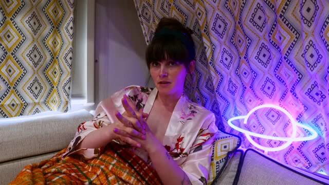 Sydney Harwin in patterned robe, purple nails, seated with expressive hands