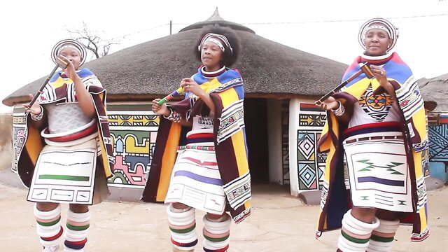 Three African Ndebele women in colorful traditional attire dancing Jerusalema challenge