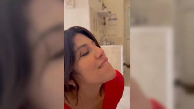 Brunette with big tits in red top smiles seductively in bath
