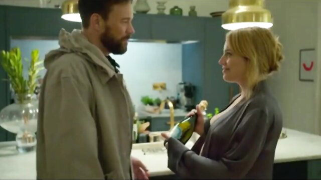 Blonde woman in gray wrap offers champagne to bearded man in kitchen, Love & Anarchy s01