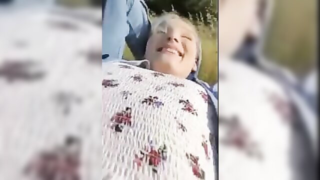 Smiling mature blonde ladyboy lying back in smocked dress outdoors