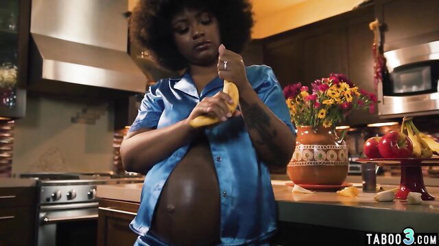 Pregnant ebony mom in silk pajamas peeling banana, craving knob