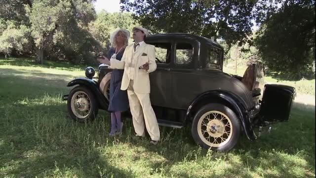 1920s gangster in cream suit with blonde in vintage dress by classic car outdoors
