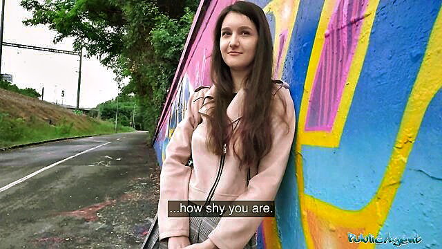 Shy 19yo college brunette in pink jacket by graffiti wall outdoors