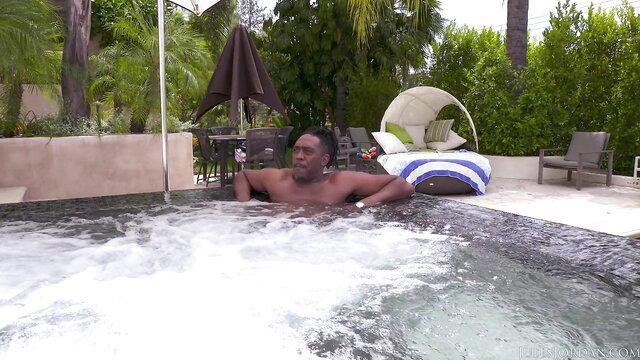 Buff black man relaxing shirtless in bubbling hot tub poolside