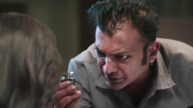 Intense Indian man in shirt holds lighter menacingly at woman in BDSM scene
