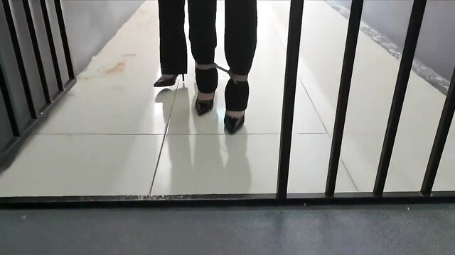 Chinese woman in black pants and heels hobbled in BDSM cuffs in prison
