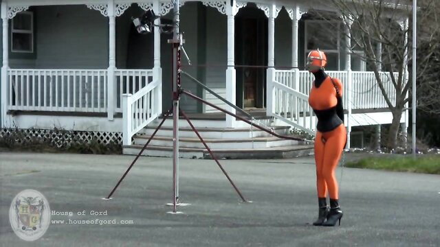 Cherry Torn in shiny orange latex catsuit outdoors BDSM tease