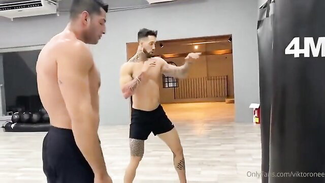Two muscular Latino hunks shirtless sparring in gym shorts